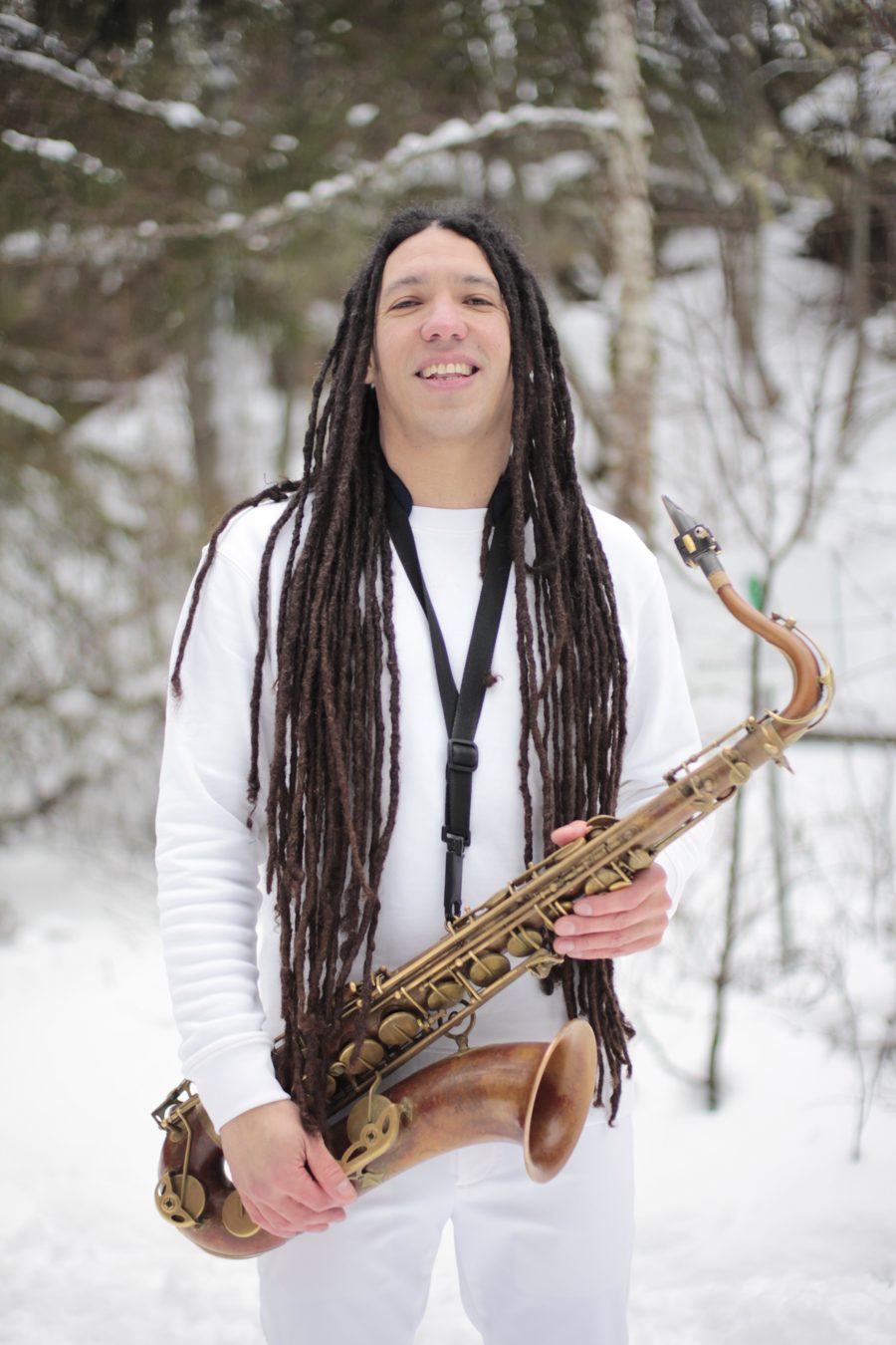Kevin Alva smiling with his tenor saxophone in a snowy forest