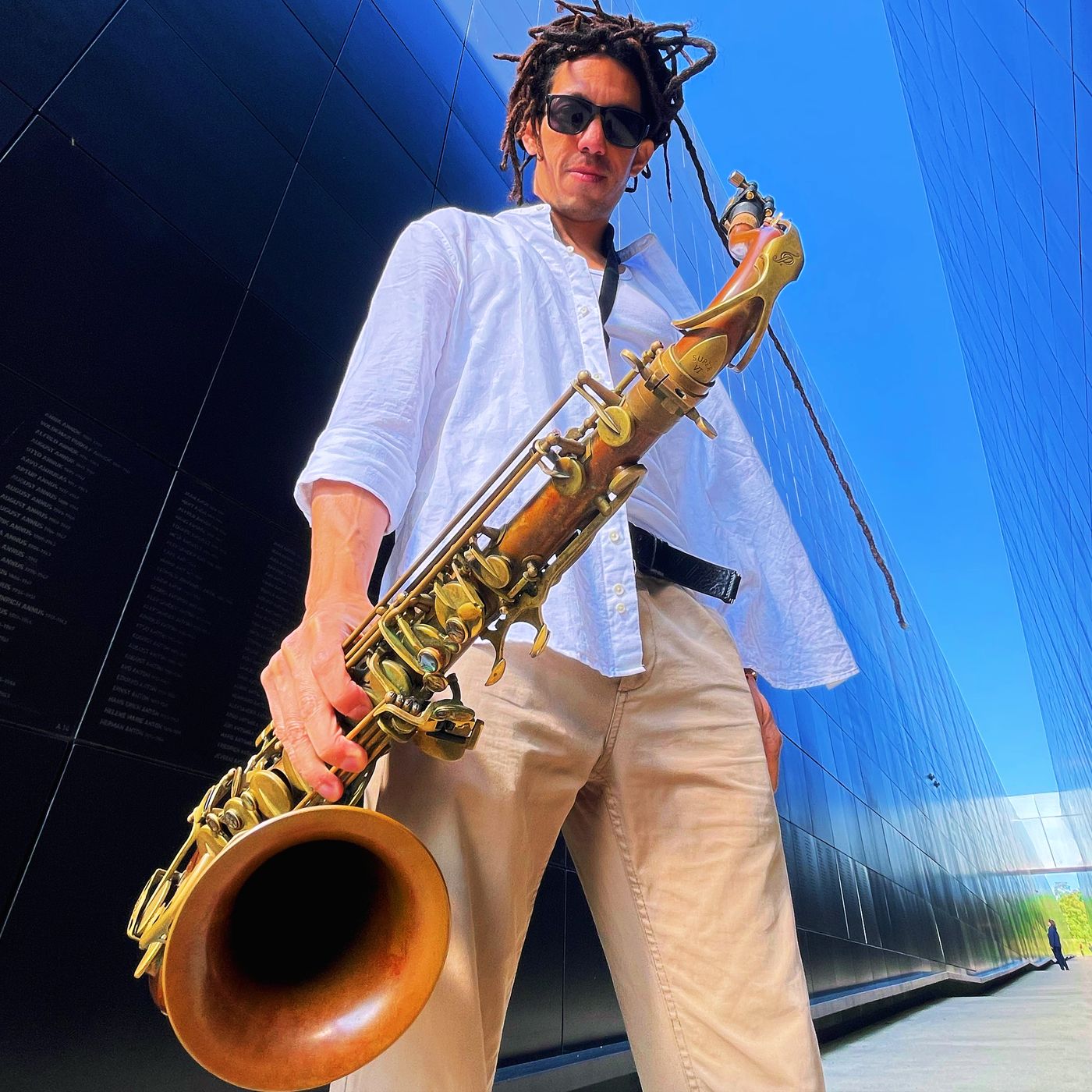 Kevin Alva with his saxophone in front of a blue wall