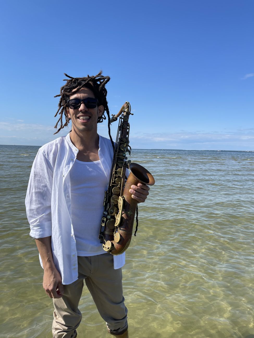 Kevin Alva smiling with his saxophone, standing in the sea